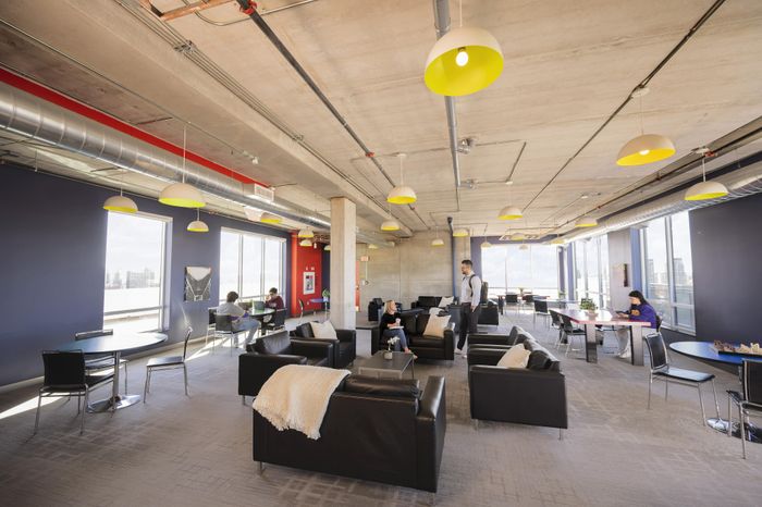 Modern open lounge space with sleek black sofas, large windows, and vibrant yellow ceiling lights creating a bright and inviting atmosphere.