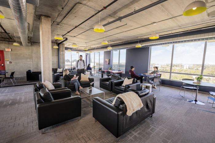 Modern communal lounge with sleek leather seating, vibrant yellow pendant lighting, and expansive city views through large windows.
