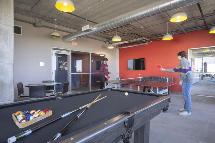 Modern recreation room featuring a sleek pool table and energetic ping pong game, highlighted by vibrant red accent wall and stylish industrial lighting.