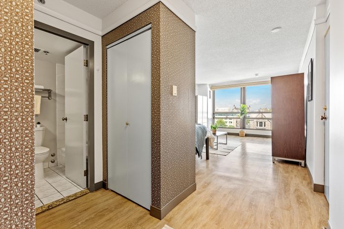 Bright and welcoming apartment hallway with elegant wooden flooring, leading to a cozy living room with large windows and a picturesque city view.