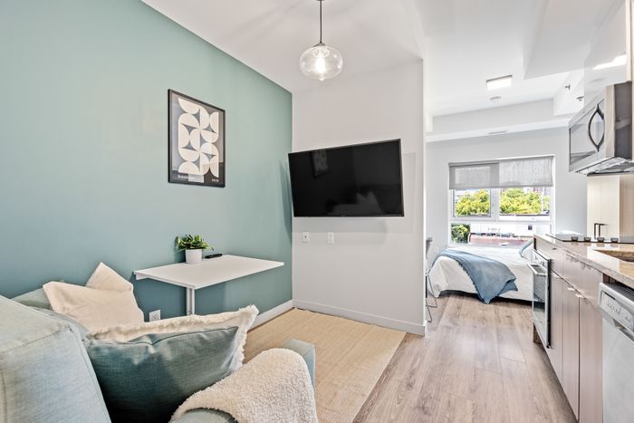 Chic modern apartment interior with cozy living area, wall-mounted TV, and a bright kitchen leading to a stylish bedroom with large windows.