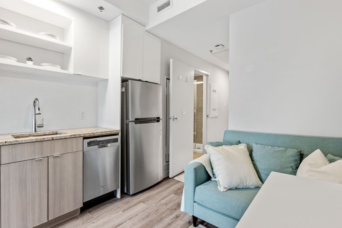 Modern apartment kitchen featuring sleek stainless steel appliances, elegant cabinetry, and a cozy seating area with a teal sofa.