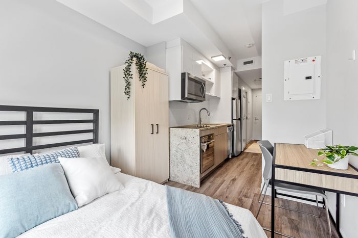 Chic studio apartment showcasing a cozy bed area, modern kitchenette with stainless steel appliances, and a stylish workspace.
