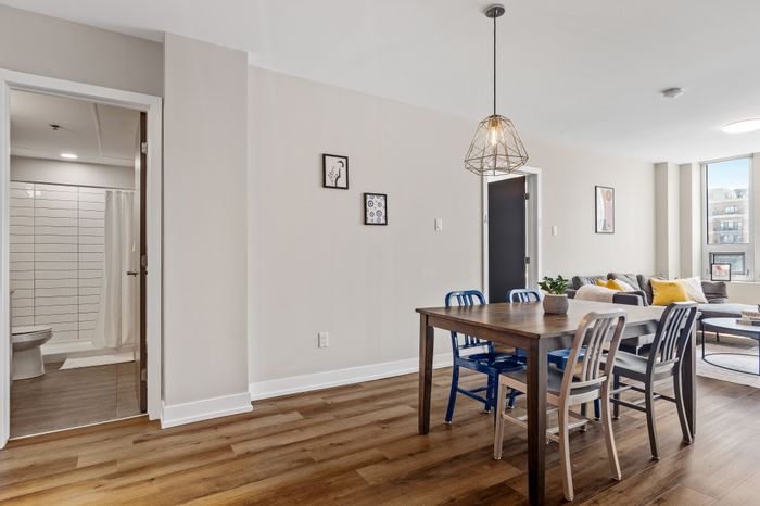 Modern apartment living area showcasing a stylish dining set, cozy lounge with vibrant pillows, and bright natural lighting, perfect for urban living.