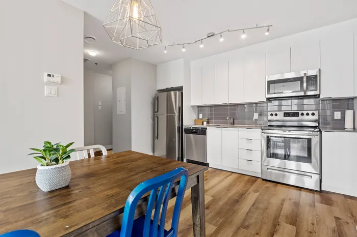 Modern kitchen with sleek white cabinetry, stainless steel appliances, and a stylish wood dining table, accented by contemporary lighting.