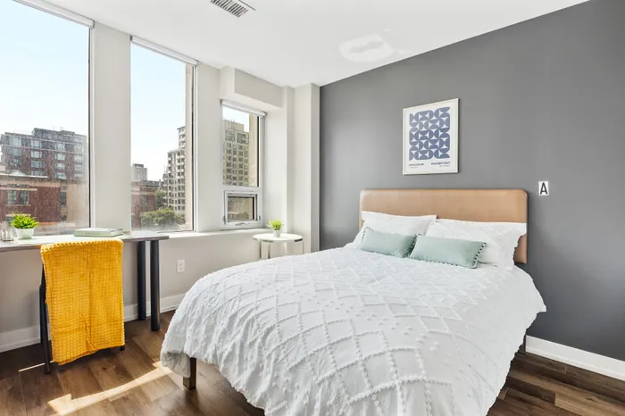 Bright and inviting bedroom with modern decor, featuring a cozy bed, large windows, and city views, perfect for a relaxing urban retreat.