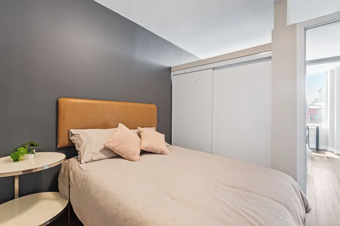 Cozy bedroom with a modern design, featuring a stylish gray accent wall, a comfortable bed with soft pillows, and a sleek side table with a touch of greenery.