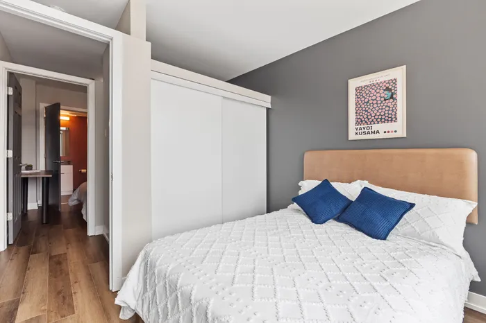 Contemporary bedroom with stylish neutral tones, featuring a cozy bed with vibrant blue cushions and modern artwork accenting the calming gray wall.