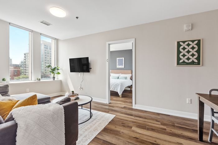 Modern living room with large windows, stylish decor, and a cozy view into a chic bedroom.