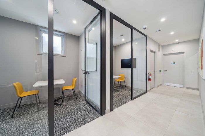 Modern office space featuring sleek glass-walled meeting rooms with vibrant yellow chairs and chic grey decor, perfect for a productive and stylish work environment.