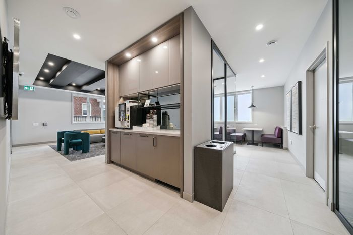 Modern apartment common area featuring a sleek coffee station, cozy seating with vibrant teal and yellow sofas, and an inviting dining nook with purple booths.