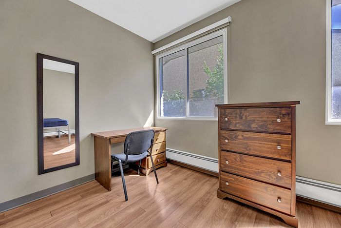 Bright, cozy room featuring a sleek writing desk, comfy chair, and elegant wooden dresser, complemented by natural light from large windows.