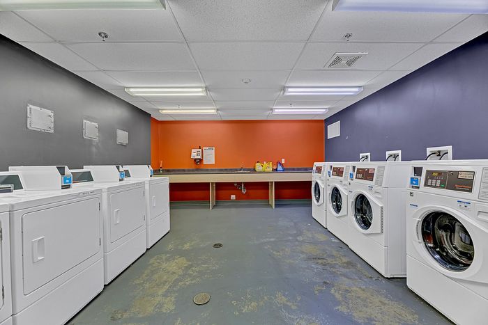 Modern apartment laundry room featuring multiple washers and dryers with sleek design under bright lighting.
