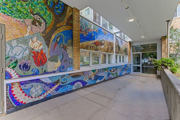Charming building entrance adorned with vibrant mosaic artwork, featuring nature scenes and abstract designs, creating a welcoming atmosphere.