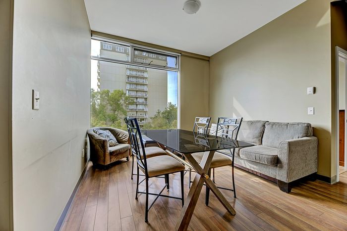 Bright apartment interior with modern dining area, elegant glass-top table, and cozy seating, featuring floor-to-ceiling windows with a view of the cityscape.