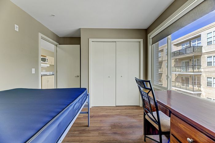 Cozy bedroom with a comfortable bed, large window offering natural light, wooden desk, and closet space, perfectly blending style and functionality.