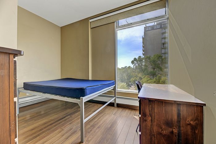 Bright and cozy bedroom with a large window offering a scenic view, featuring a minimalist metal bed and a stylish wooden desk.