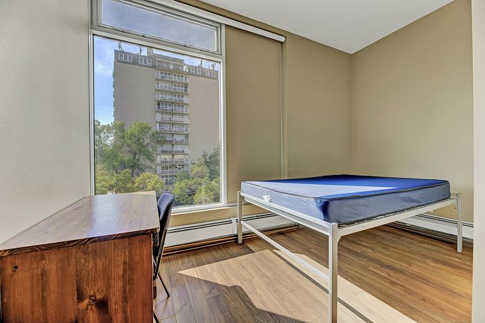 Bright bedroom with large window offering scenic city views, featuring sleek wooden floors and minimalist furniture.