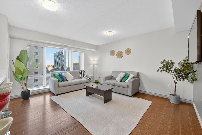Bright and modern living room with large window view, cozy gray sofas, vibrant green and blue cushions, elegant wooden floor, and stylish decor accents.