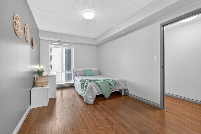 Bright and airy bedroom with modern decor, featuring sleek hardwood flooring, a cozy bed with soft green accents, and natural light pouring in from a large window.
