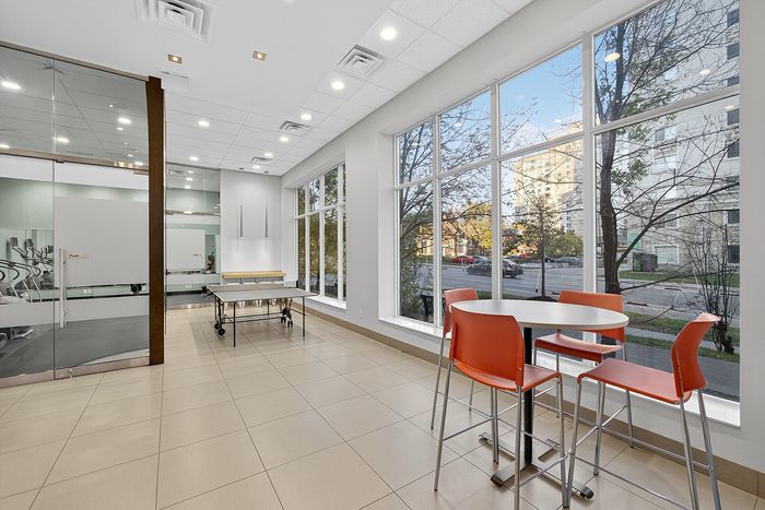 Bright, modern lounge area with large windows, a ping pong table, and vibrant orange chairs, perfect for relaxation and socializing.