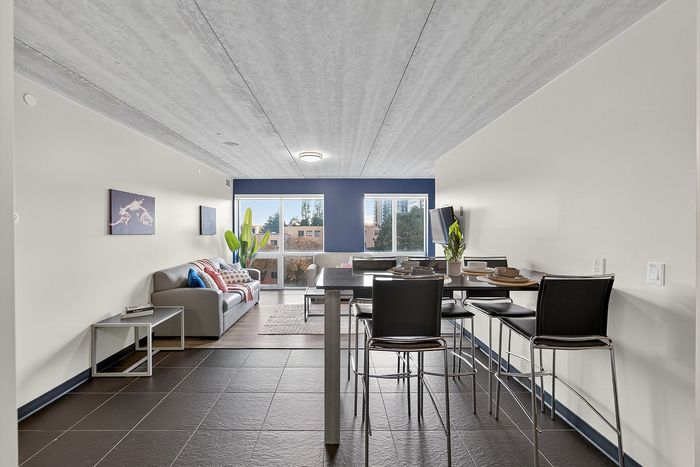 Modern open-plan living and dining area with elegant furnishings, large windows offering natural light and a chic urban view.