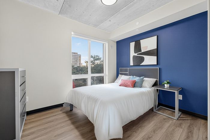 Bright, modern bedroom featuring a cozy bed, stylish artwork, and large window with scenic view.