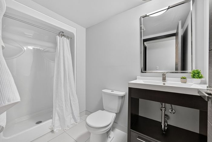 Modern bathroom featuring sleek fixtures, a large mirror, and elegant shower area with crisp white curtains.