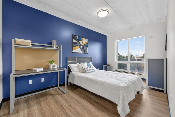 Modern bedroom with a sleek design, featuring a comfortable bed, stylish desk, and large window offering a serene view.