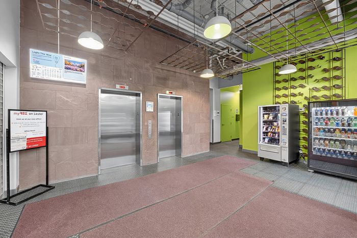 Contemporary lobby with dual elevators, vibrant green walls, and convenient vending machines, creating a welcoming atmosphere.
