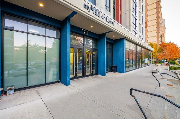 Inviting entrance of a modern building with bold blue accents, large glass windows, and a vibrant autumn backdrop, showcasing a blend of urban and natural beauty.