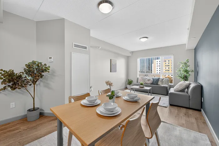 Bright and modern open-concept living area featuring a stylish dining table, cozy seating, and large windows with a city view.