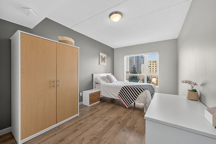 Bright and modern bedroom featuring stylish wood flooring, a comfortable bed with chic accents, and a large window offering stunning city views.