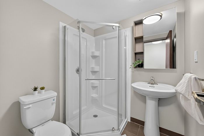 Modern bathroom with sleek glass shower, elegant pedestal sink, and stylish wall-mounted mirror, complemented by tasteful decor and ceramic flooring.