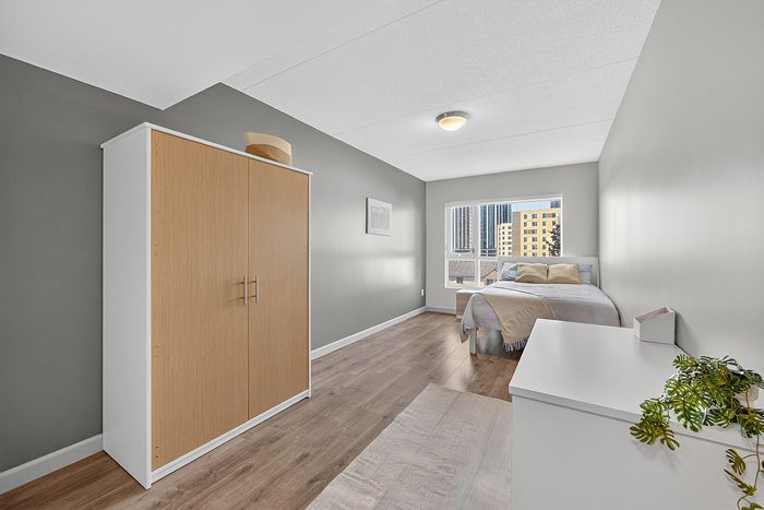 Bright and modern bedroom with sleek flooring, elegant wardrobe, and large window offering stunning city views.
