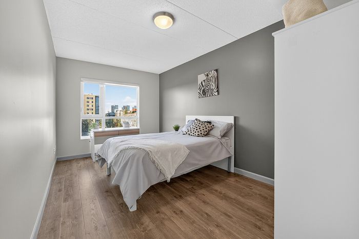 Bright and modern bedroom with chic decor, featuring wood flooring and a large window with urban views.