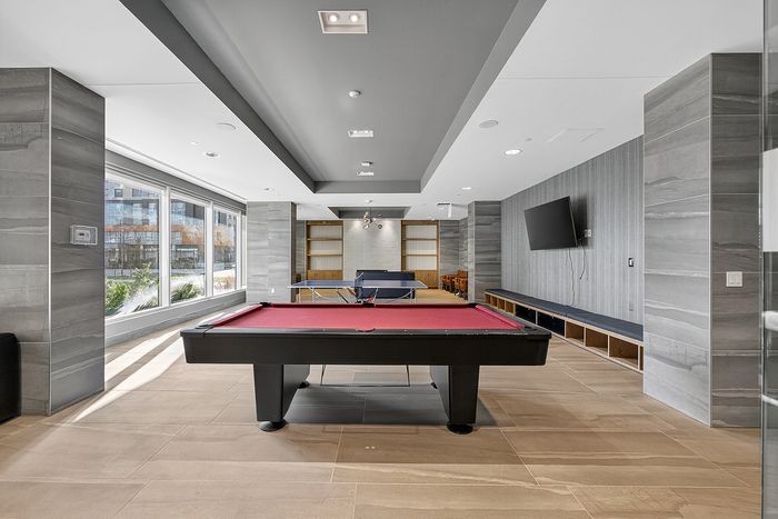 Elegant recreation room featuring a sleek pool table, modern decor, and large windows offering abundant natural light.