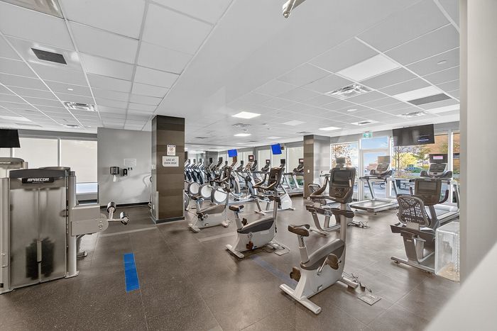 Modern apartment gym with high-end exercise equipment, abundant natural light, and sleek interiors.