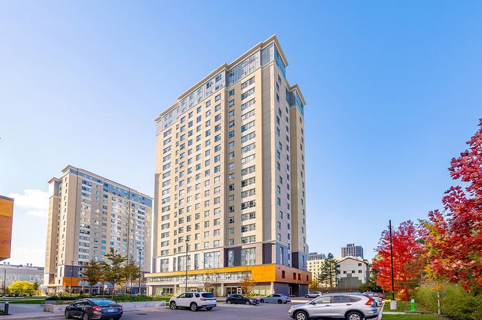 Modern high-rise apartment building with expansive windows, surrounded by vibrant autumn foliage and a clear blue sky, offering urban living at its finest.