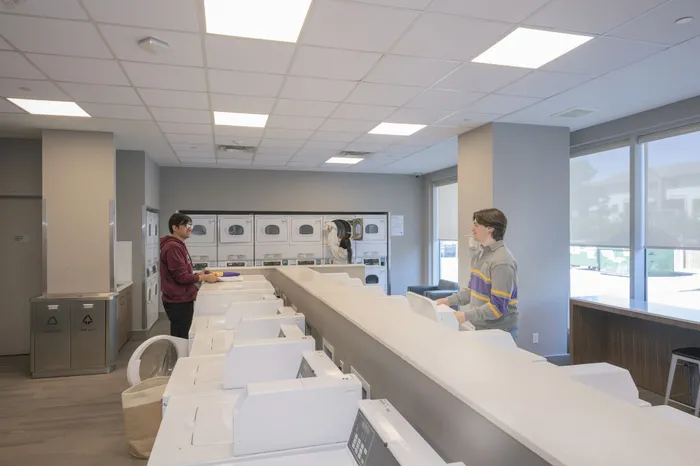 Modern and spacious laundry room with multiple washers and dryers, featuring bright lighting and large windows for a welcoming atmosphere.