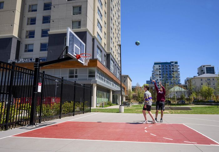 Vibrant outdoor basketball court with players enjoying a game, set against a modern apartment building and clear blue skies.