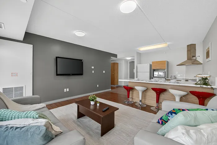 Modern open-concept living room with cozy seating, sleek wall-mounted TV, and stylish kitchen island with vibrant red bar stools.