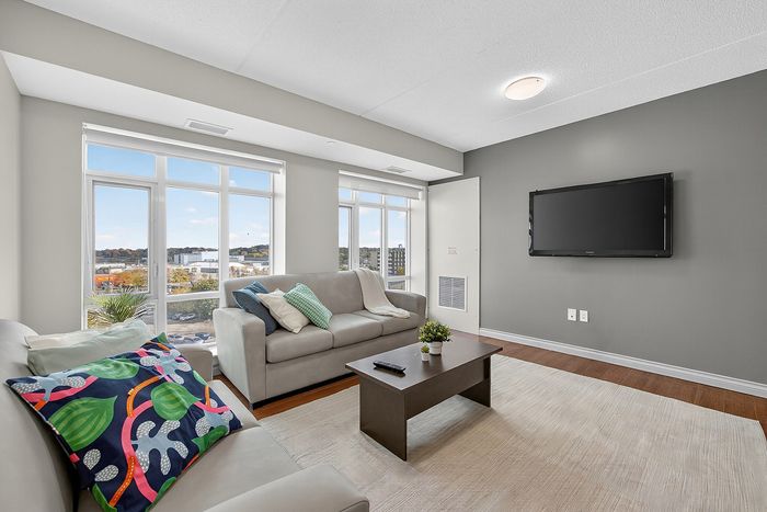 Bright and modern living room with large windows, stylish sofas, and a sleek wall-mounted TV, offering a cozy and inviting atmosphere.