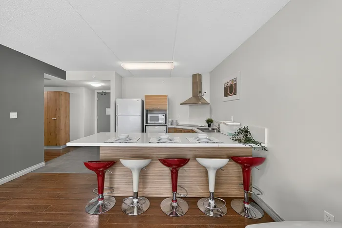 Modern kitchen with sleek countertops, vibrant red and white bar stools, stainless steel appliances, and elegant wooden flooring.