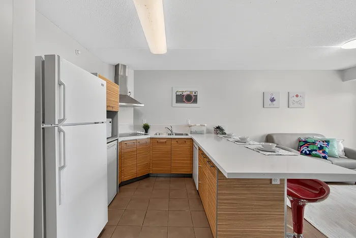 Contemporary kitchen with sleek appliances, wood cabinetry, and an inviting breakfast bar leading to a cozy living area.