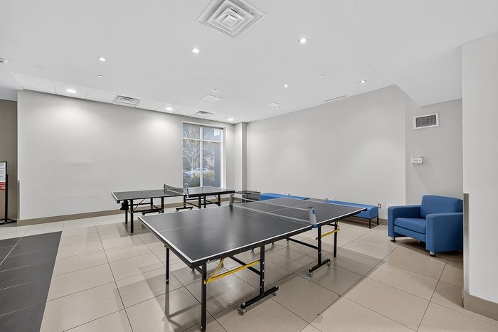 Modern recreation room with dual table tennis setup, bright lighting, and cozy seating for relaxation.