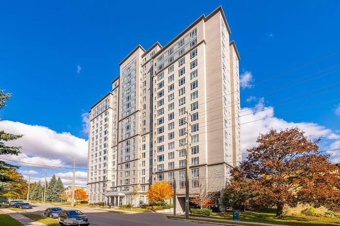 Modern high-rise apartment building with numerous windows and elegant architecture, surrounded by vibrant autumn trees under a bright blue sky.