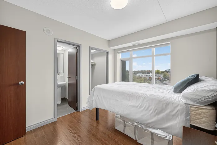 Bright, modern bedroom with large windows offering a scenic view, featuring a cozy bed and access to an ensuite bathroom.