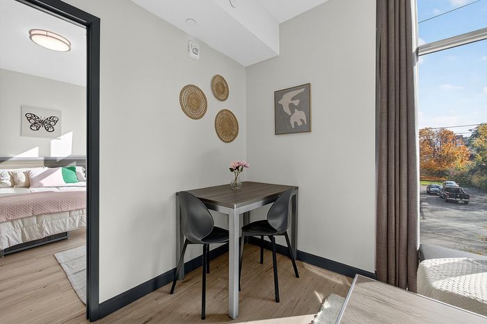 Cozy dining nook with chic wall decor and black chairs next to a bright bedroom view, perfect for relaxed living.