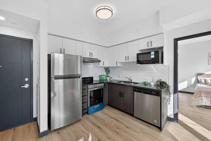 Modern kitchen with sleek stainless steel appliances, elegant cabinetry, and stylish wood flooring leading to a cozy bedroom with natural light.
